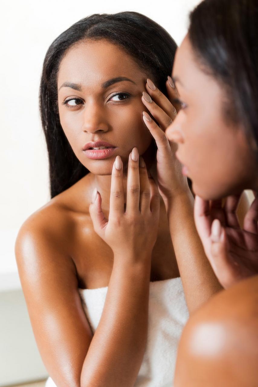 woman examining her skin while looking in the mirror